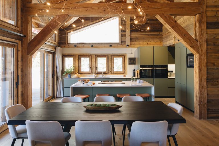 Aménagement Morel d'une cuisine vert sauge avec grand îlot central et salle à manger dans un luxueux chalet en bois massif.