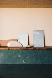 Carreaux et pièces en céramique aux teintes terracotta, blanc et bleu posés sur une tablette en bois, au-dessus d'un plan en pierre vert profond