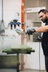 Artisan Morel appliquant au pistolet une teinte vert sur-mesure sur une façade, cabine de laquage de l'atelier breton