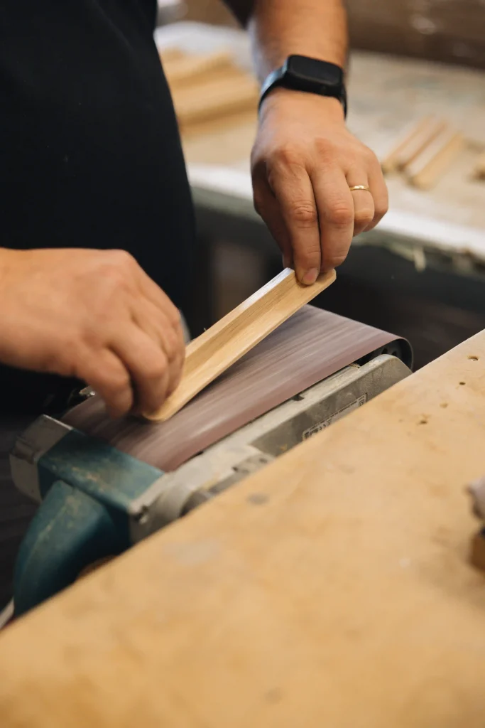 Artisan Morel ponçant à la main une poignée en bois sur une ponceuse à bande, atelier de fabrication en Bretagne