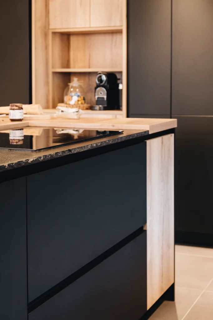 Cuisine bois Morel mêlant façades noir mat et bois clair, îlot avec plan en pierre foncée et niche coin café
