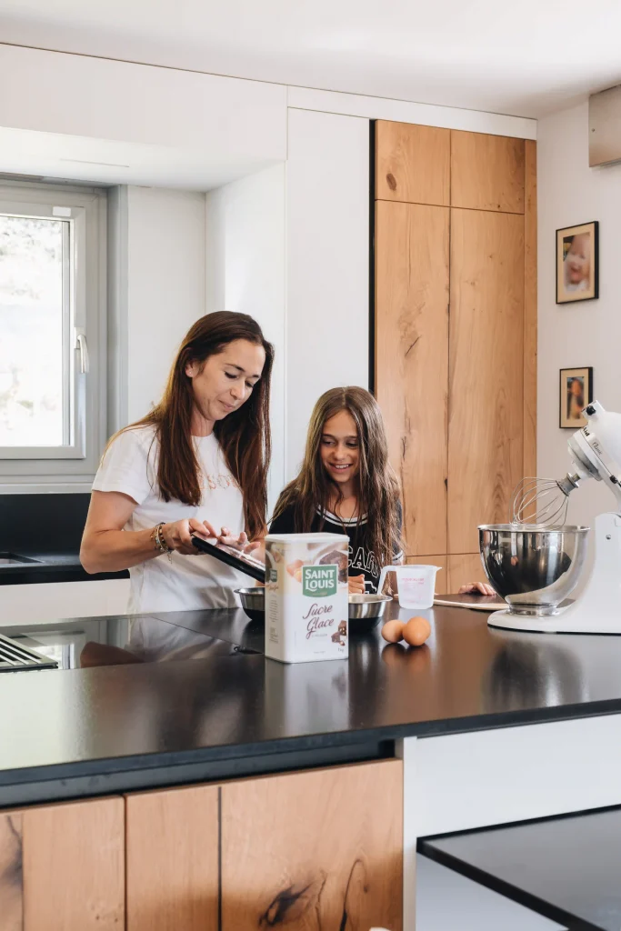 Mère et fille pâtissant ensemble dans une cuisine bois Morel en chêne clair avec plan de travail noir et îlot