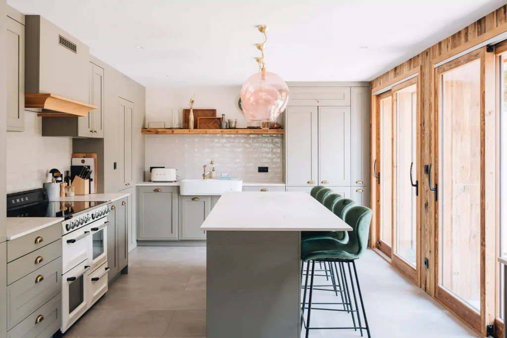 Cuisine Morel de style cottage aux façades bois laqué gris-vert à cadre, îlot en pierre, piano SMEG et grandes baies en bois