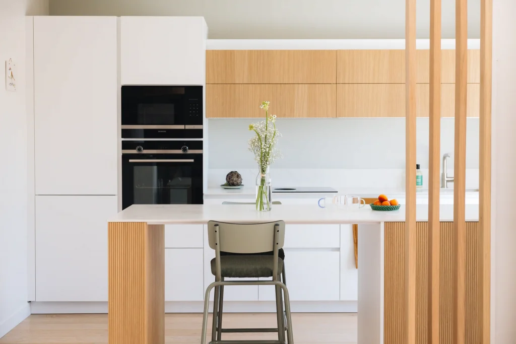 Cuisine bois moderne Morel mêlant façades blanches mates et bois clair strié, avec îlot-bar et claustra en bois