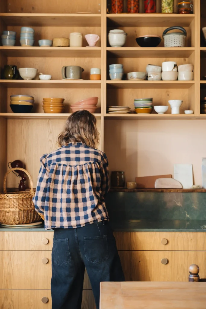 Marion Graux devant ses étagères de cuisine garnies de céramiques aux teintes bleu, rose, ocre et vert