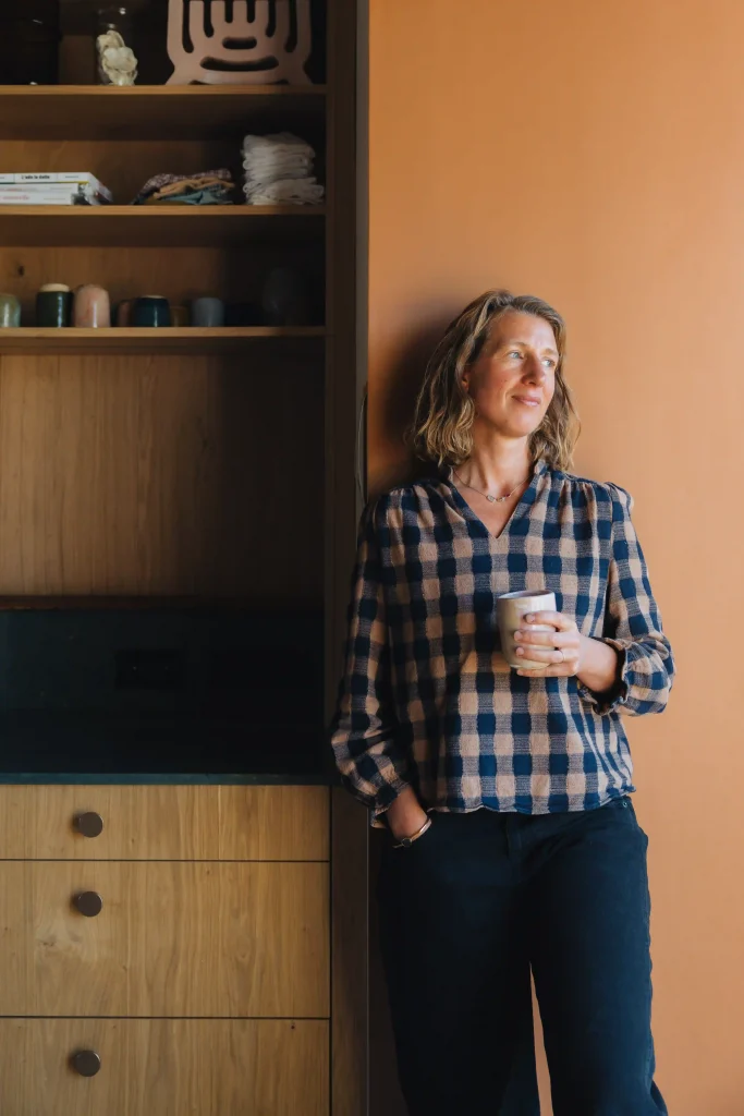Portrait de la céramiste Marion Graux adossée à un mur terracotta, une tasse en grès à la main