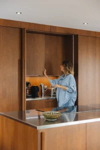 Cuisine bois moderne Morel en noyer avec meuble à coulisse dissimulant un coin café et un plan de travail inox