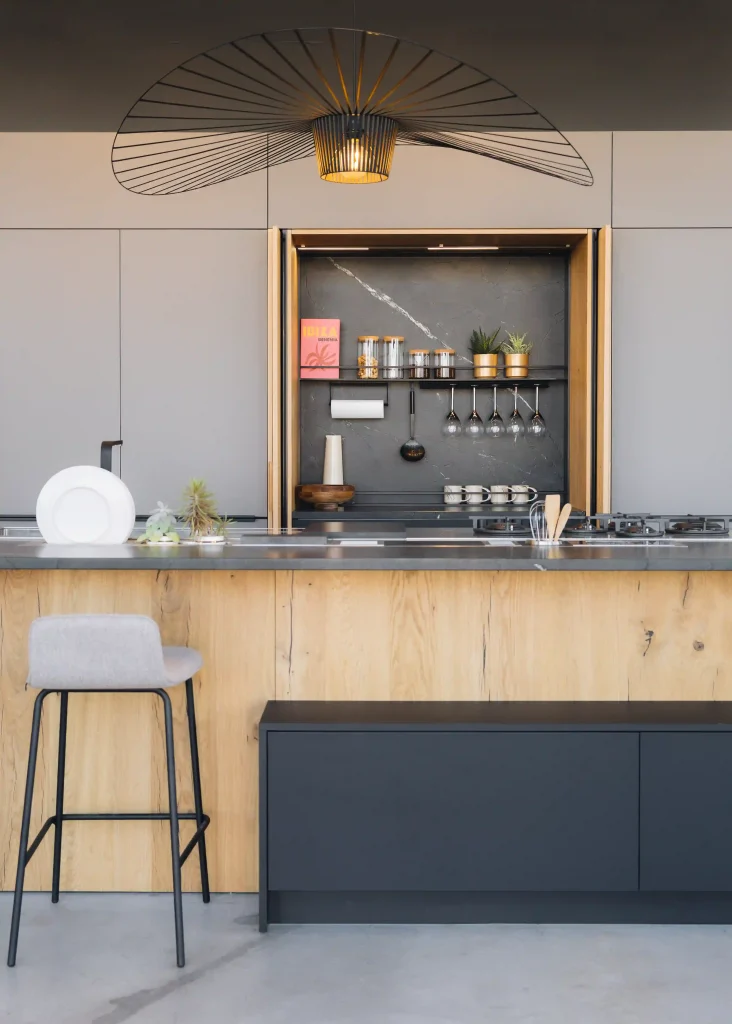 Cuisine bois Morel en chêne clair avec façades grises, niche escamotable en marbre gris et grande suspension design