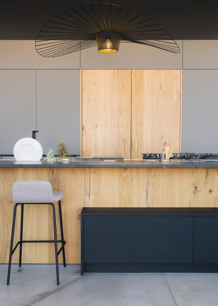 Cuisine bois Morel en chêne clair avec façades grises, îlot gris anthracite, plan en pierre et grande suspension design