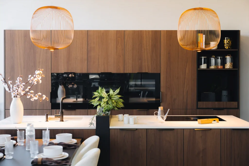Cuisine bois moderne Morel en noyer avec grand îlot, plan de travail clair, électroménager noir encastré et suspensions dorées