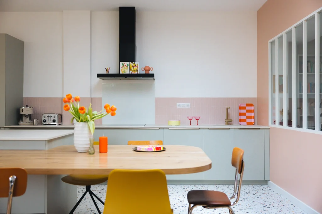 cuisine vert de gris avec crédence et mur rose poudré, plan de travail clair et sol terrazzo